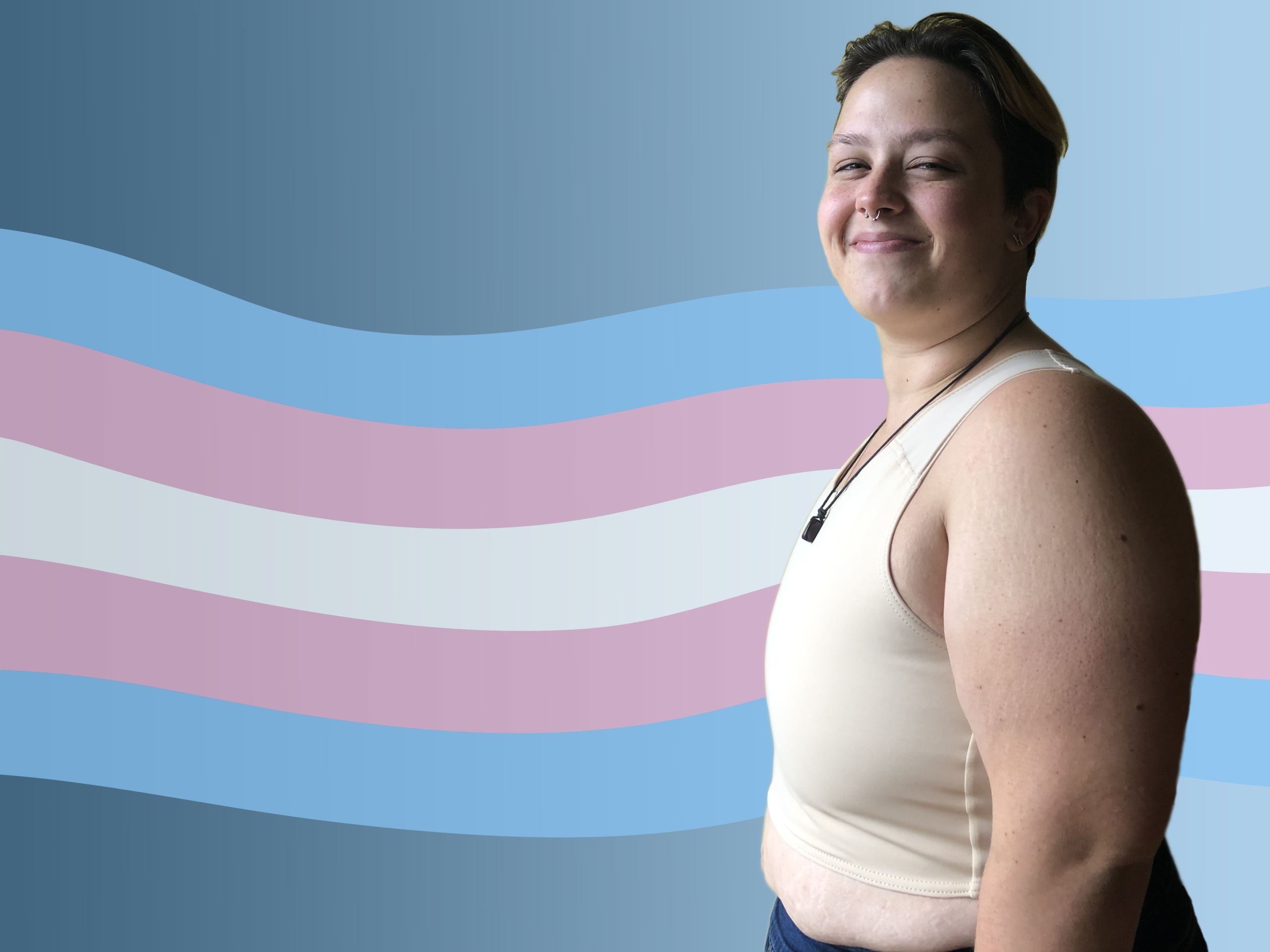 A trans person wearing a white binder smiles at the camera. A white, pink and blue trans flag waves across the background.