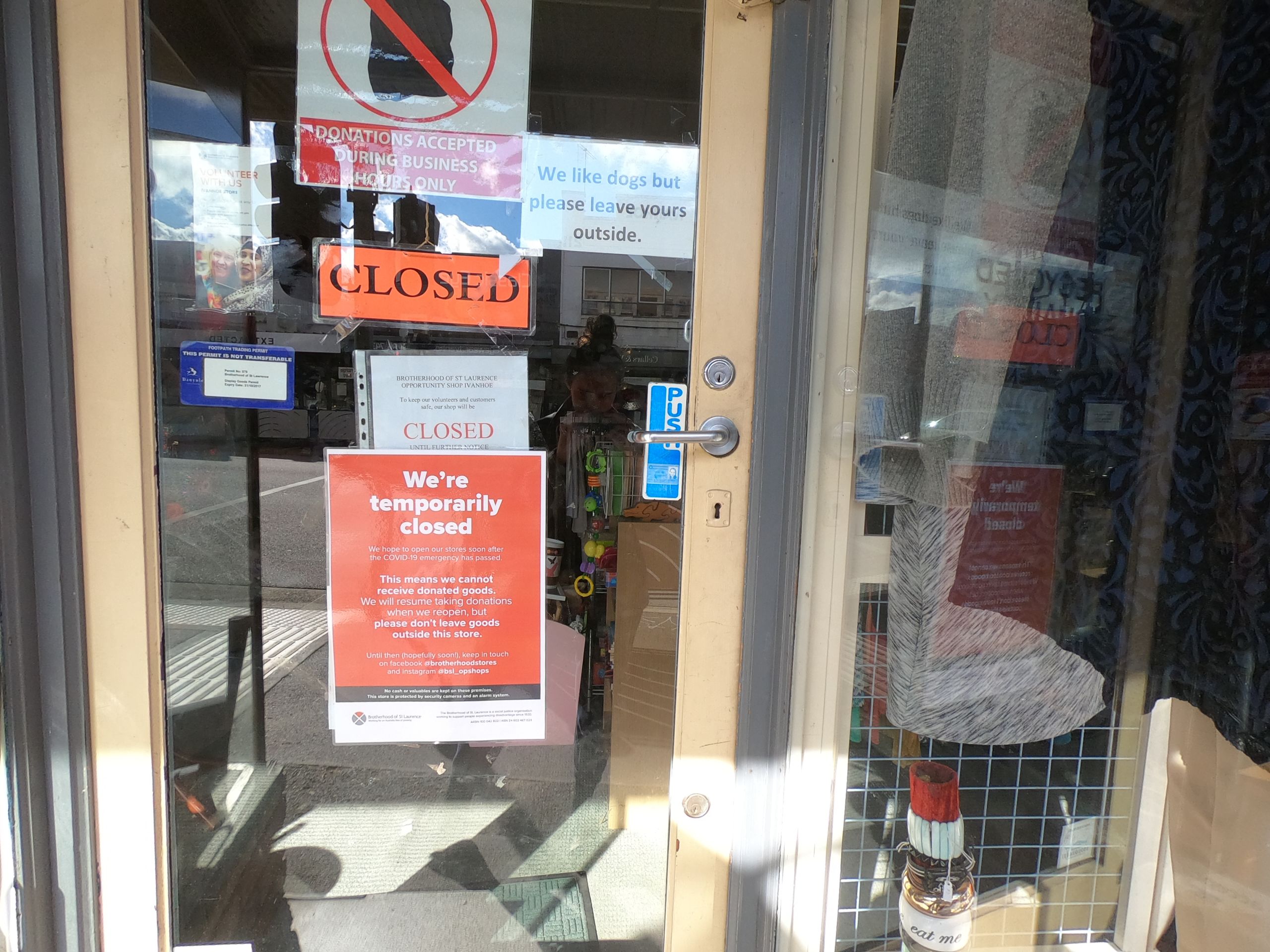 Multiple signs on an op-shop door reading "CLOSED", "CLOSED", "We're temporarily closed".
