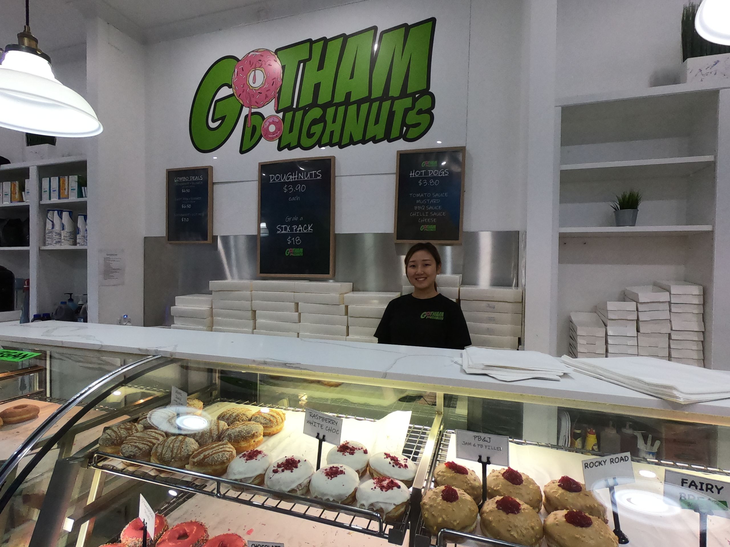 Maho, the staff member at Gotham Doughnuts who has worked with George through the pandemic, smiling and standing behind one of the doughnut cabinets in the store.